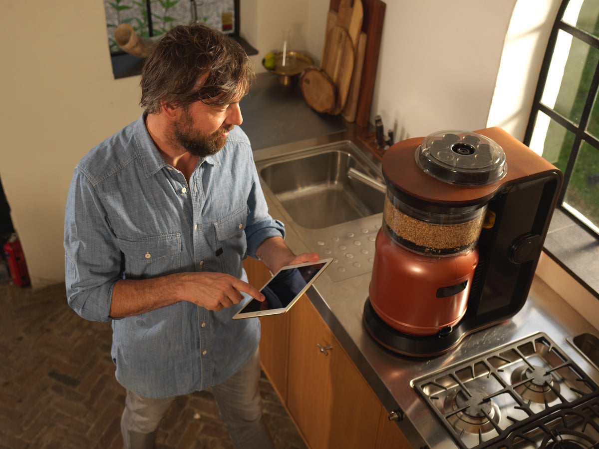 A brewer checks his MiniBrew from a tablet, grain in the mash tun, hop carousel on top